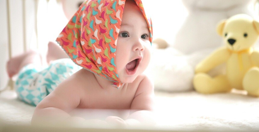 a baby laughing on a bed after having bath with teddy bears on the side
