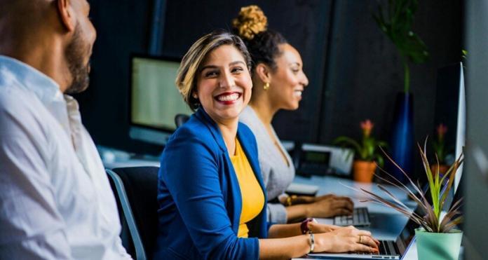a lady marketer laughing with a man and another lady working on the laptop in office