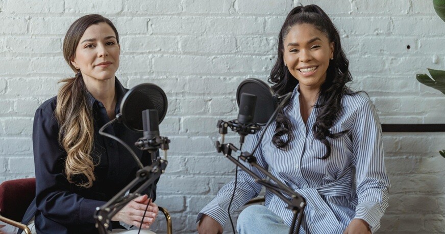 podcast two ladies talking over mikes in a podcast setting