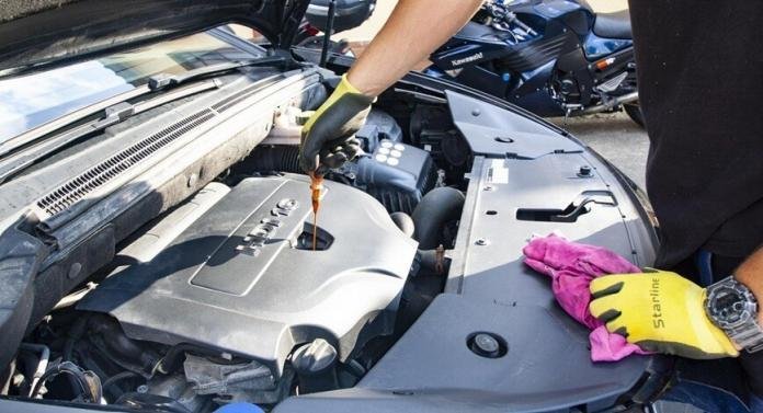 a mechanic repairing a car engine wearing a glove on the bonnet