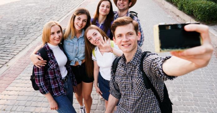 A group of young students on an educational trip stand together on a cobblestone sidewalk to take a selfie.