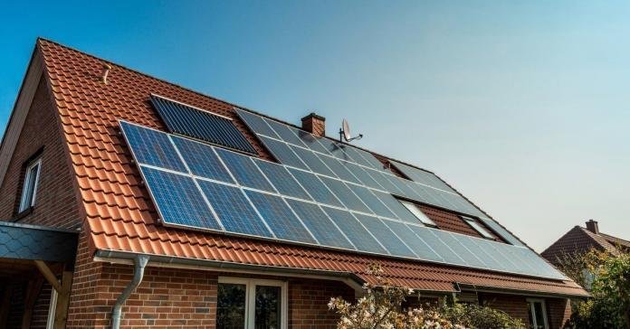 A large one-story house with a sloped roof covered in clay shingles with multiple rows of solar panels under the sun.