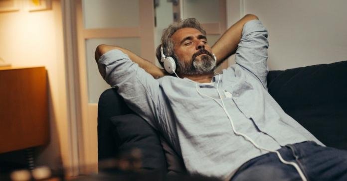 A middle-aged person relaxing on a lounging chair at home while listening to music using over-ear headphones.